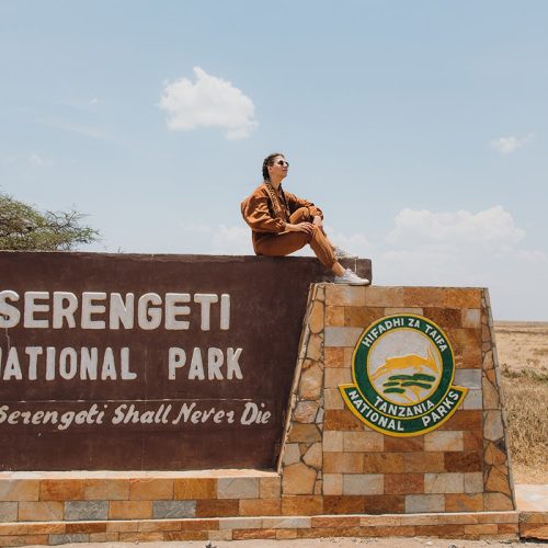 A-young-woman-sitting-on-the-stone-signboard-of-Serengeti-National-Park-Tanzania